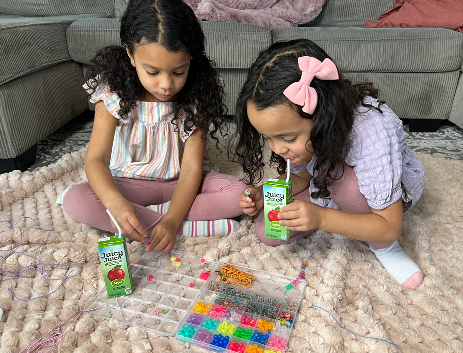 young children drinking juicy juice looking at freind ship bracelets beads and strings