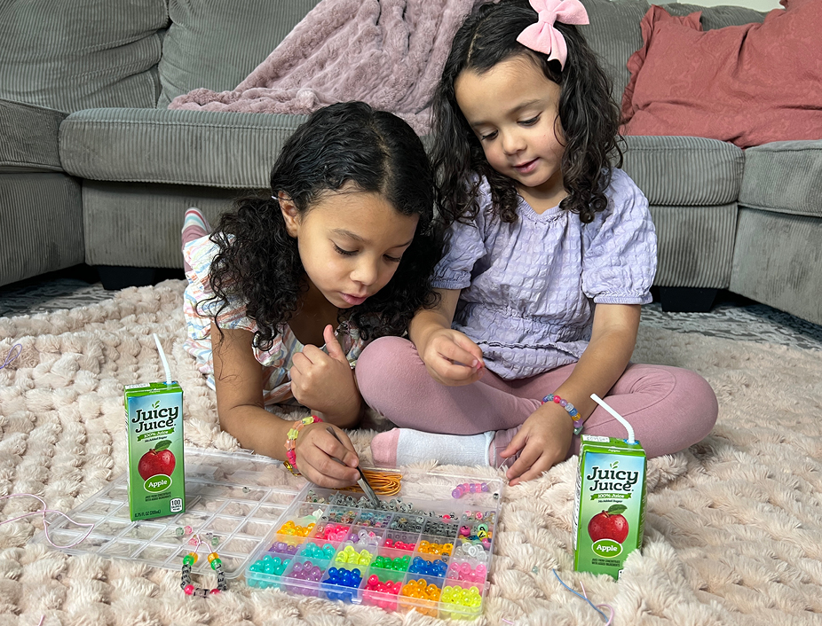 young children drinking juicy juice looking at freind ship bracelets beads and strings