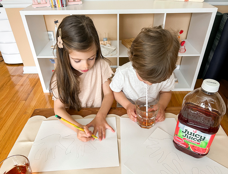 Young children tracing their hands with the pencil on white paper and drinking Juicy Juice 100% juice